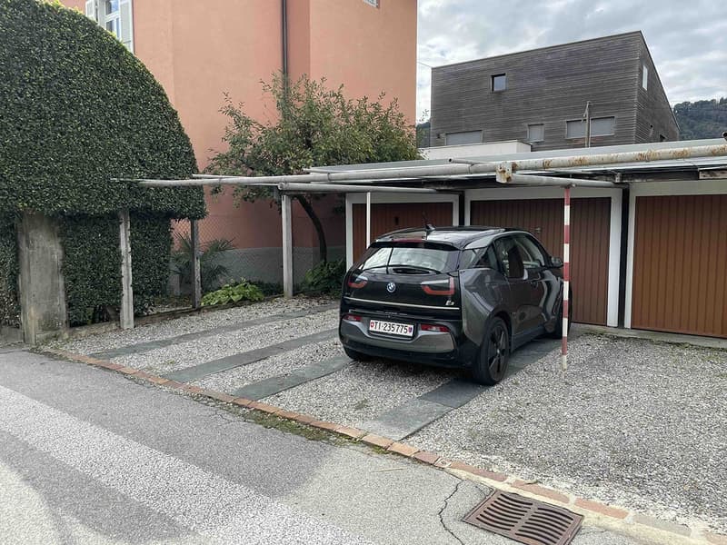 black BMW electric car parked under a cover in a shared parking area with gravel and plants