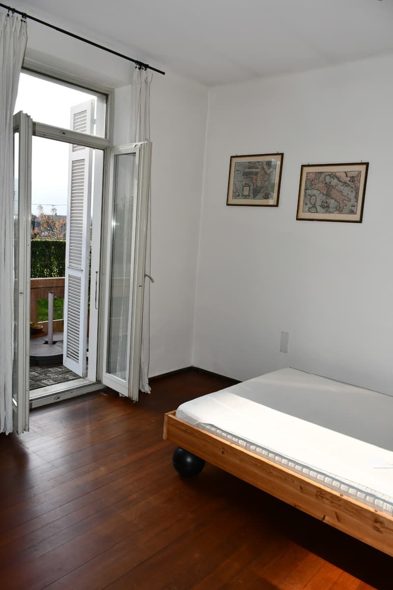An empty room with a bed, wooden floor, two open glass doors, and a white sheet.