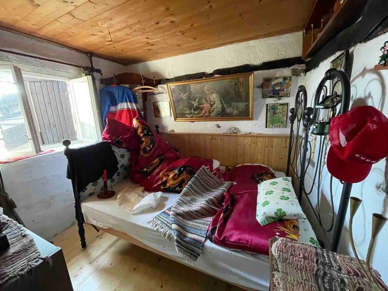 Wooden bed with white sheets, pillows, and blankets, wooden wall, wooden window, painting, hat, lamp