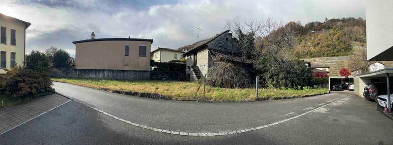 Undeveloped land with several houses on the side of the road, a parked car in a garage, and two cars parked in front.