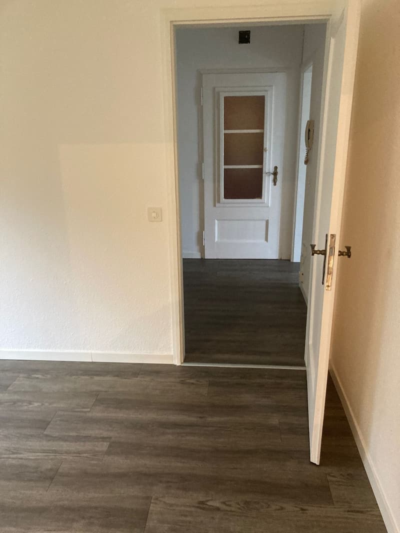 Empty hallway, wooden floor, white walls, open door, closed door with glass window