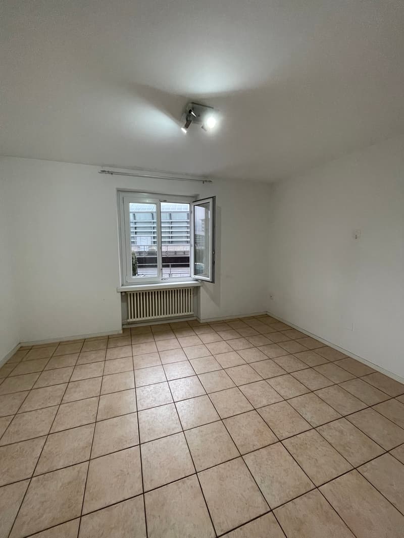 Empty room with beige tiles, white walls, large window, white radiator, light fixture