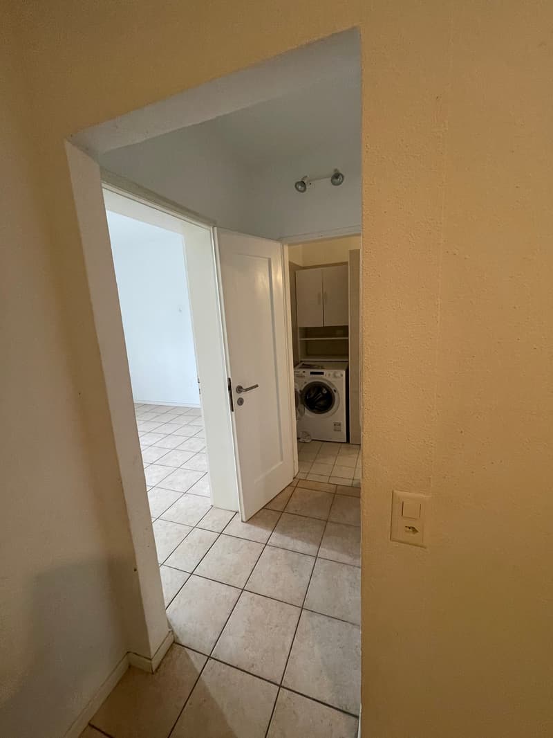 An empty room with a tiled floor, an open door, a washing machine, and cabinets.