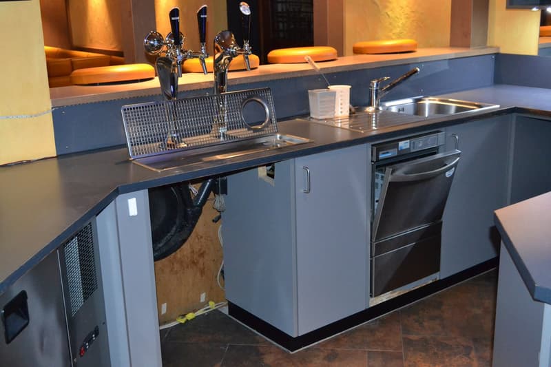 Modern kitchen with stainless steel sink, faucet, and dishwasher. Dark countertops and cabinets. Tile flooring.