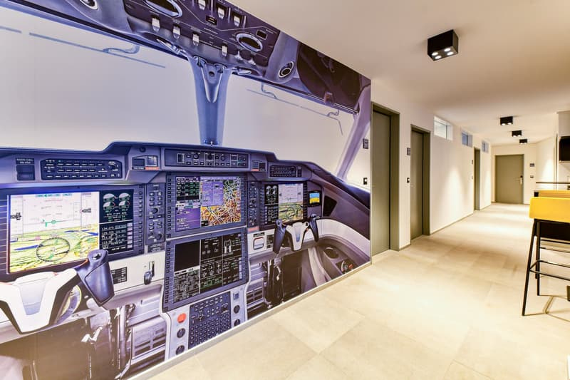 A corridor with a mural depicting an airplane cockpit, beige tiled floor, and a few lit ceiling lights.