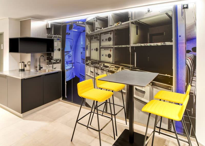 Compact kitchen with integrated sink, yellow bar stools, tiled floor, countertop table, large wall mural