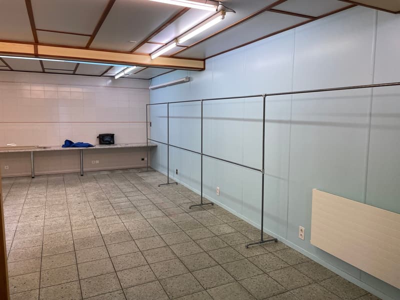 Open space, tiled flooring, metal frames, light fixtures, white tiles, counter, black bag, power outlets, heater