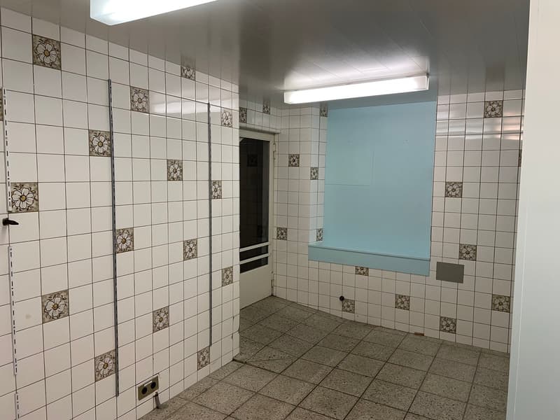 The image shows a bathroom with white tile walls featuring floral patterns, a blue vanity, and a tiled floor.