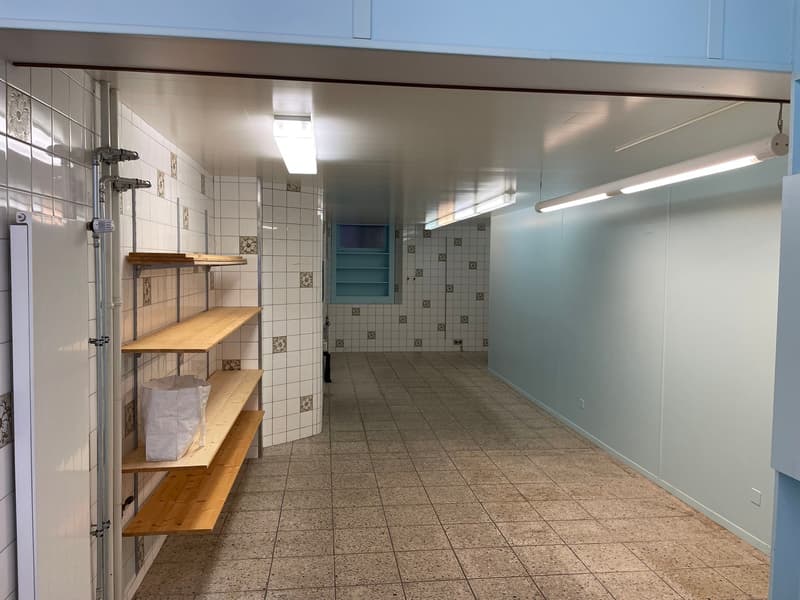 The image shows a basement or storage area with tiled floors, white walls, and wooden shelving units. The space appears to be well-lit with fluorescent lighting and has a clean, utilitarian feel.