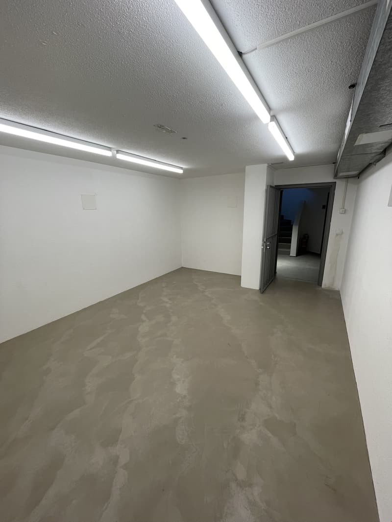 large, empty room, concrete floor, bright fluorescent lights, single exit
