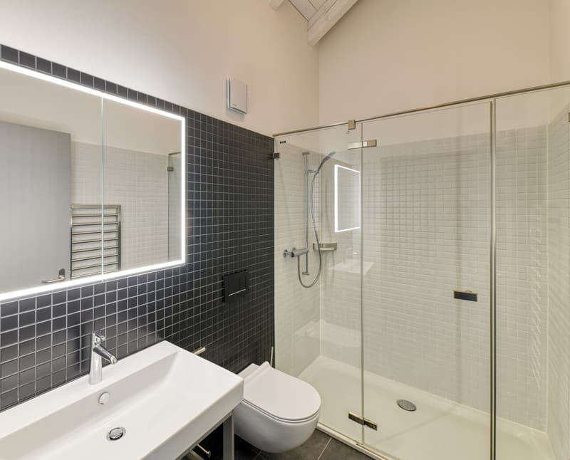 white sink, white toilet, modern shower with glass enclosure, mirror with light, tiled walls