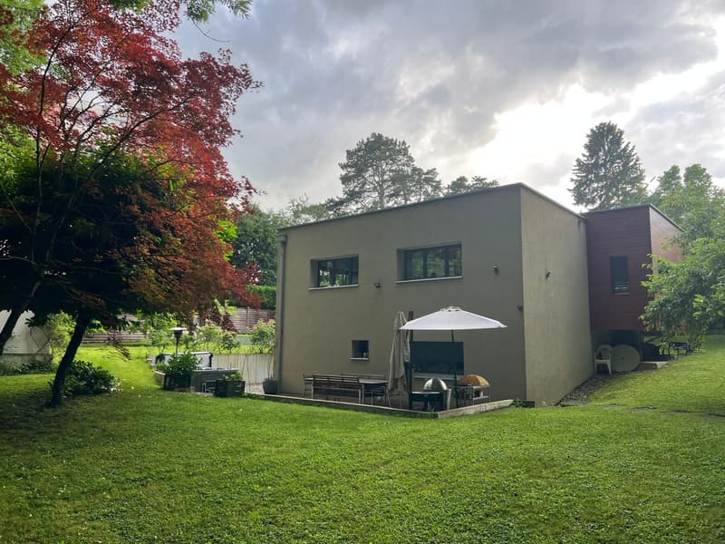 modern house, gray exterior, large windows, outdoor seating area, umbrella, garden, trees