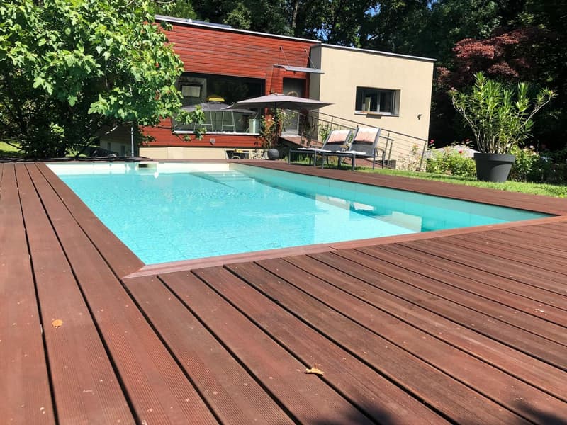 Swimming pool with wooden deck, lounge chairs, umbrellas, and plants