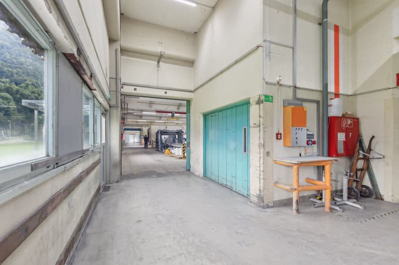 The image shows a large, open industrial space with high ceilings, concrete floors, and various equipment and machinery visible. There is a green painted door in the background, and a fire extinguisher and other equipment can be seen in the foreground.