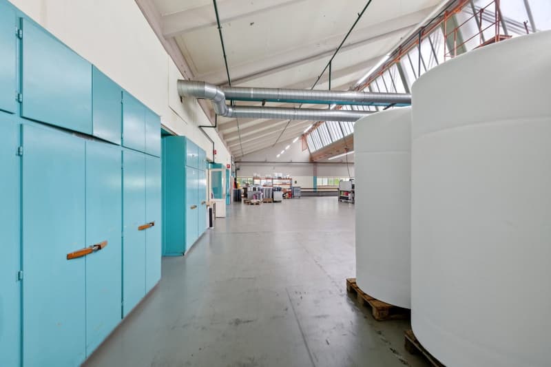 Large open space with high ceilings, concrete floors, and exposed ductwork. The space appears to be used for storage or industrial purposes, with blue lockers or storage units along one wall.
