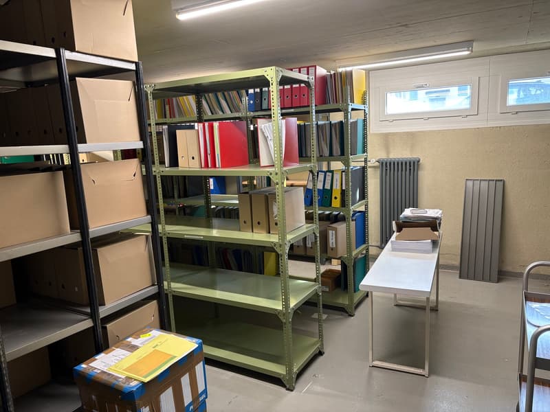 storage area with metal shelves, stacks of storage boxes, a wooden desk, and office supplies on shelves