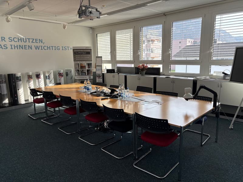 large room with meeting table, chairs, whiteboard, cabinets, projector, flowers, carpet