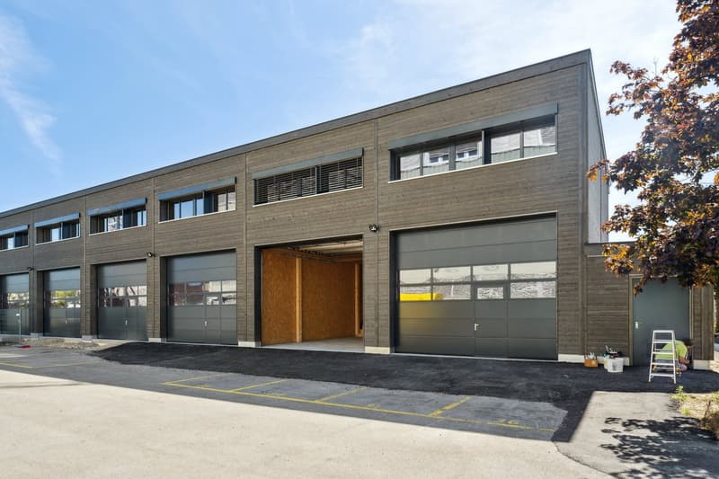 Industrial building with multiple garages, gray exterior, windows, and an open garage door.