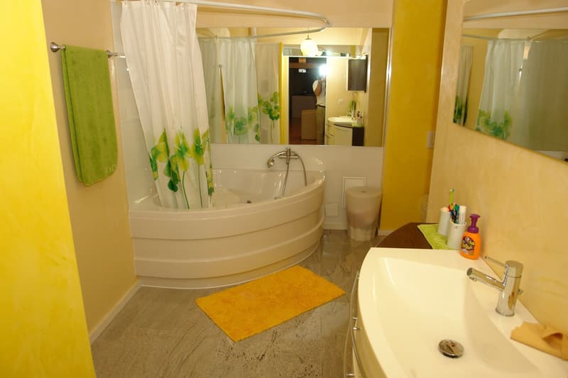 Bathroom with a large bathtub, sink, mirror, and yellow rug. The walls are painted yellow, and there is a towel hanging on the wall.