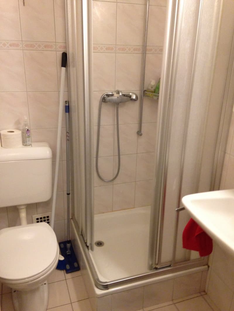 white tiled walls, white toilet, shower with glass door, white sink, red towel