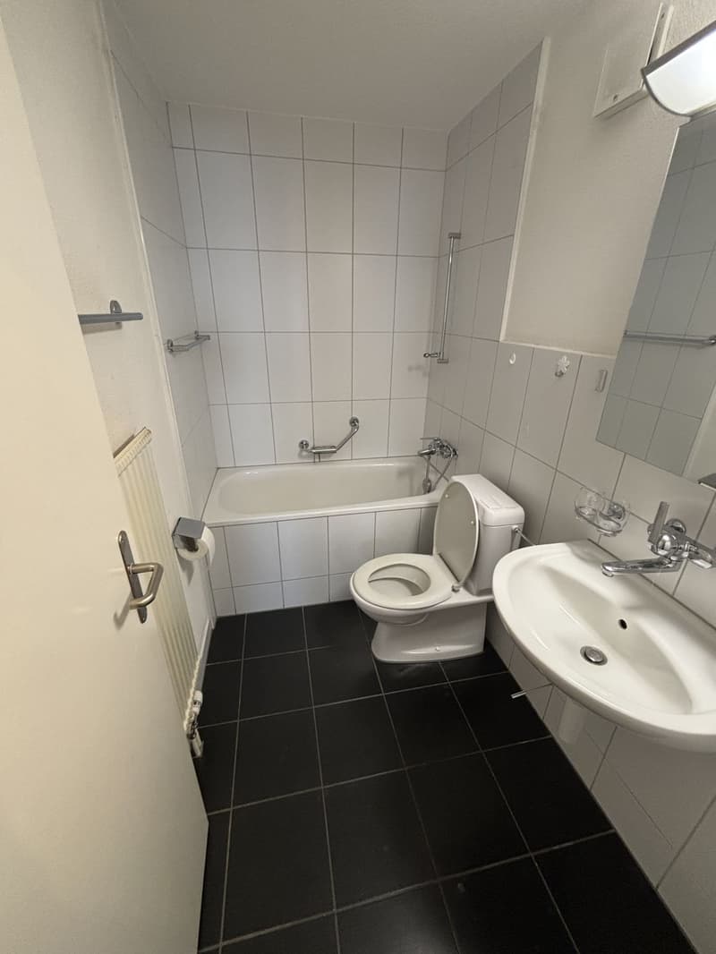 Bathroom with white tiles, white bathtub, white toilet, white sink, mirror, and radiator