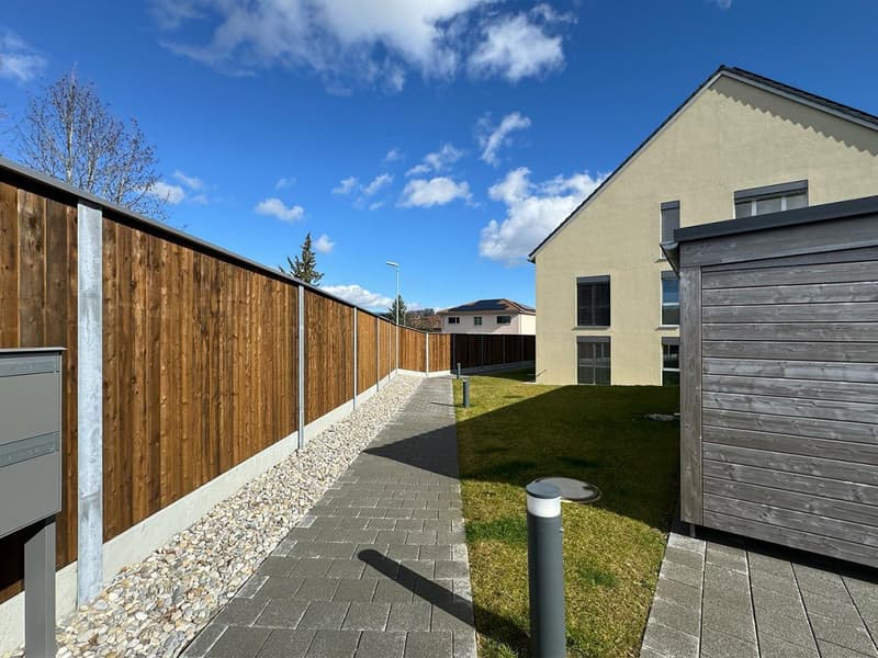 Backyard of a house with wooden fence, paved pathway, and mailbox.