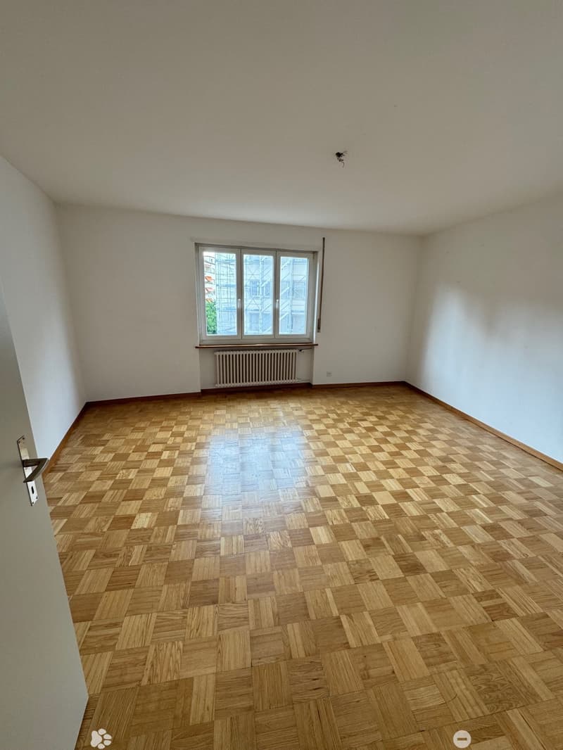 Empty room with white walls, large windows, and a parquet wood floor in a checkered pattern.