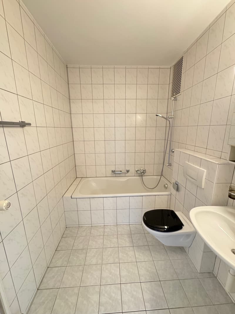 Tiled bathroom with a bathtub, shower, toilet, and vanity. The walls are covered in white tiles arranged in a grid pattern.