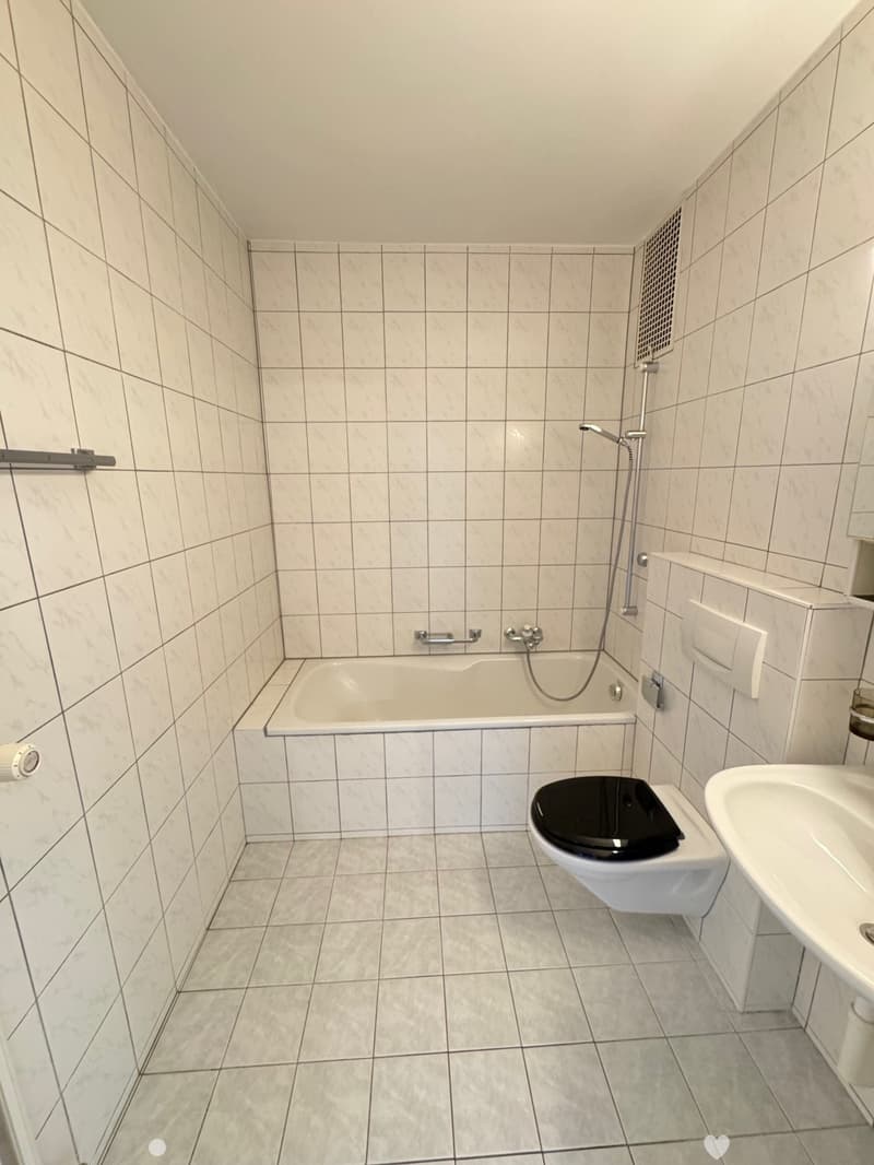 Tiled bathroom with a bathtub, shower, toilet, and vanity. The walls are covered in white tiles arranged in a grid pattern.