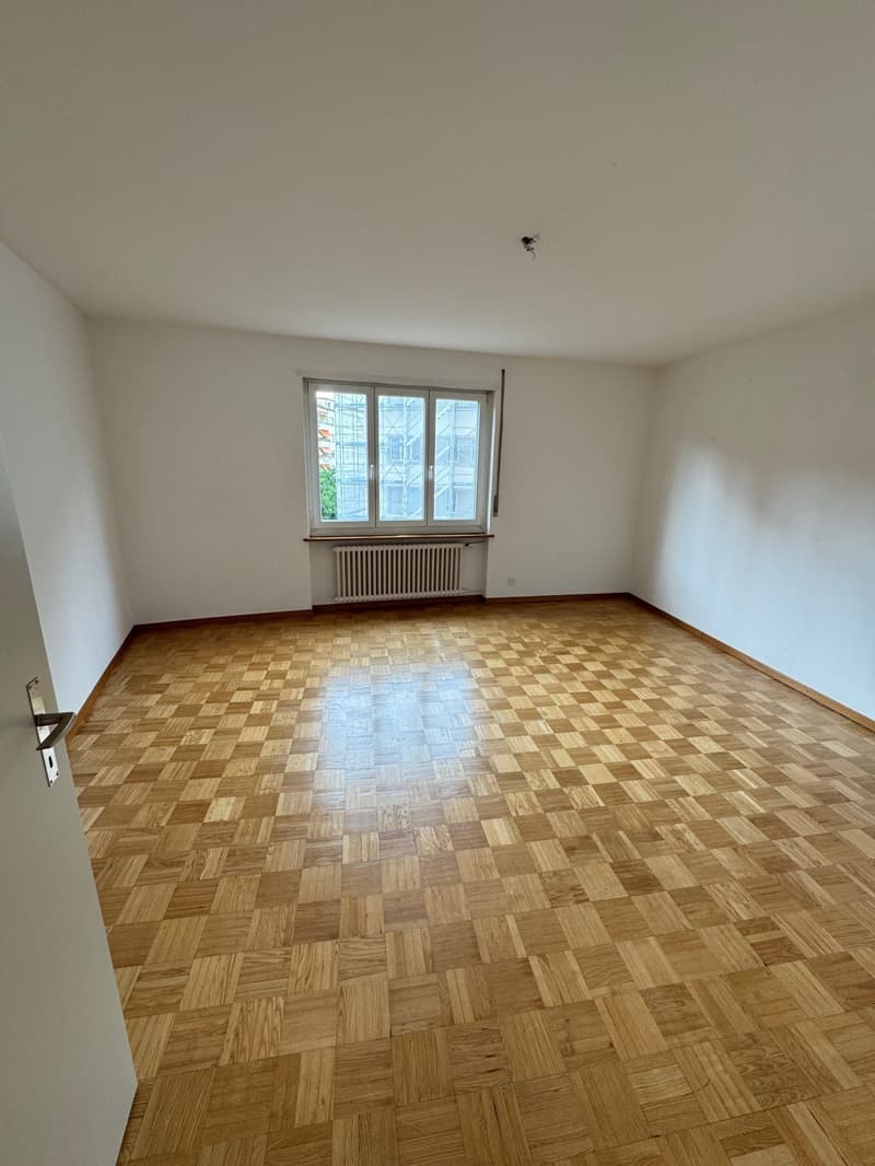Empty room with white walls, large windows, and a parquet wood floor in a checkered pattern.
