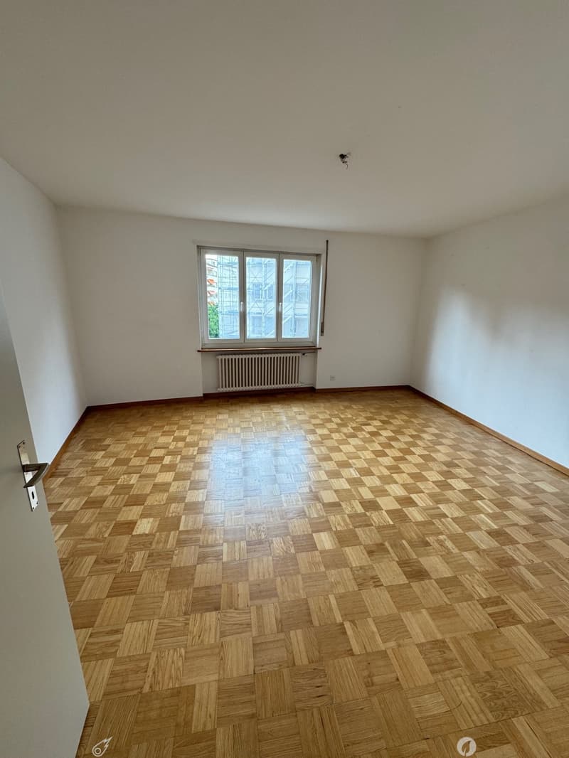 Empty room with white walls, large windows, and a parquet wood floor in a checkered pattern.