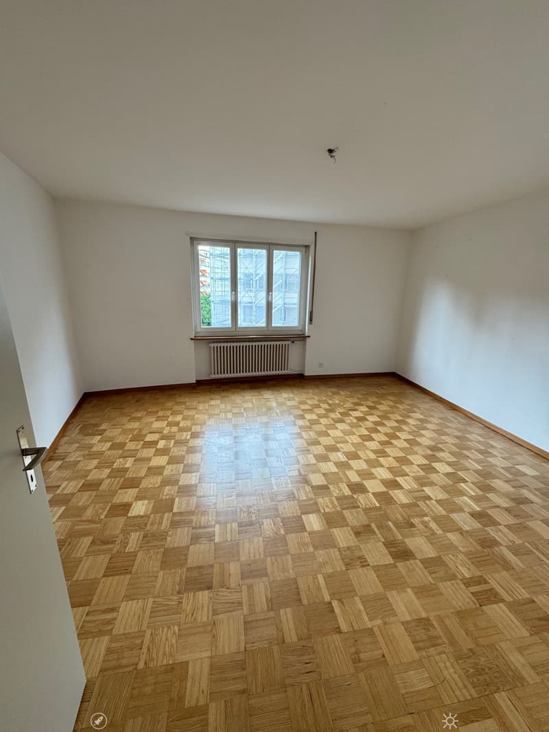 Empty room with white walls, large windows, and a parquet wood floor in a checkered pattern.