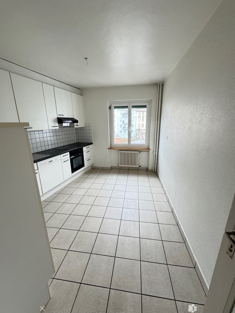 The image shows a kitchen with white cabinets, a tiled floor, and a window overlooking the exterior. The kitchen appears to have a stove, oven, and other appliances.