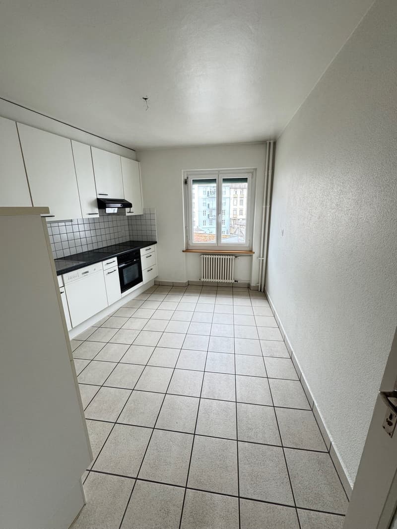 The image shows a kitchen with white cabinets, a tiled floor, and a window overlooking the exterior. The kitchen appears to have a stove, oven, and other appliances.