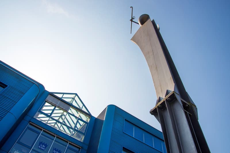 A modern, blue-colored building with large glass windows and a distinctive architectural feature on top, possibly a sculpture or decorative element.