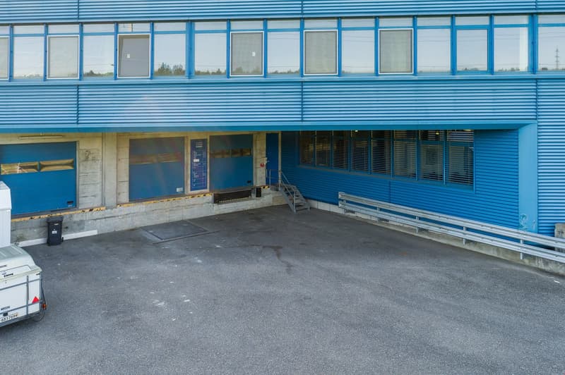 A large blue commercial building with multiple windows and a paved parking area in front.