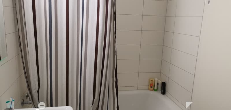 Bathtub, sink, white tiles, shower curtain, bottles on the ledge