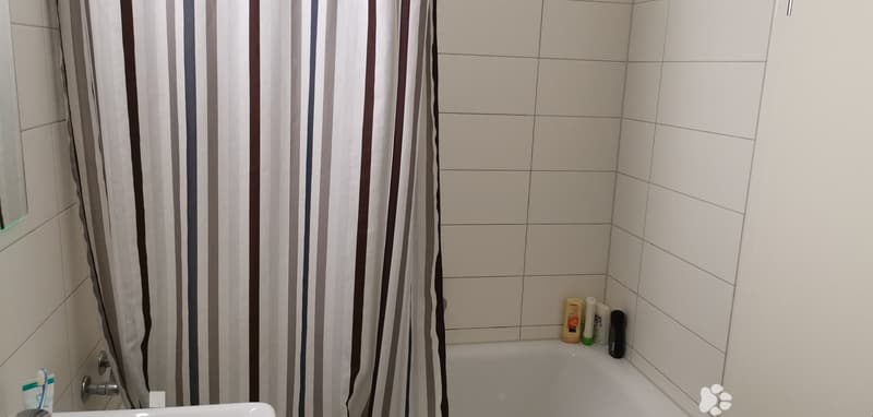 Bathtub, sink, white tiles, shower curtain, bottles on the ledge