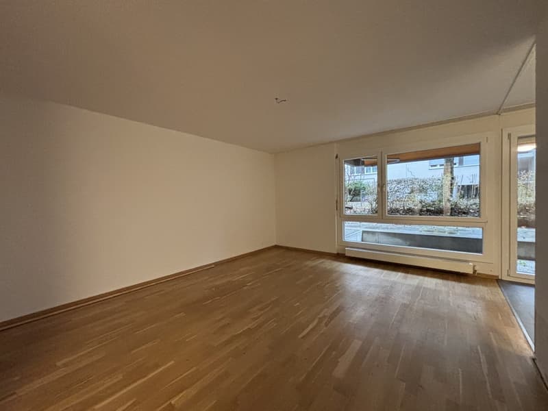 Empty room, hardwood floors, white walls, large windows with external view
