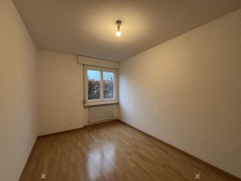 Empty room with wooden floors, white walls, single window with white frame, ceiling lamp, white radiator.