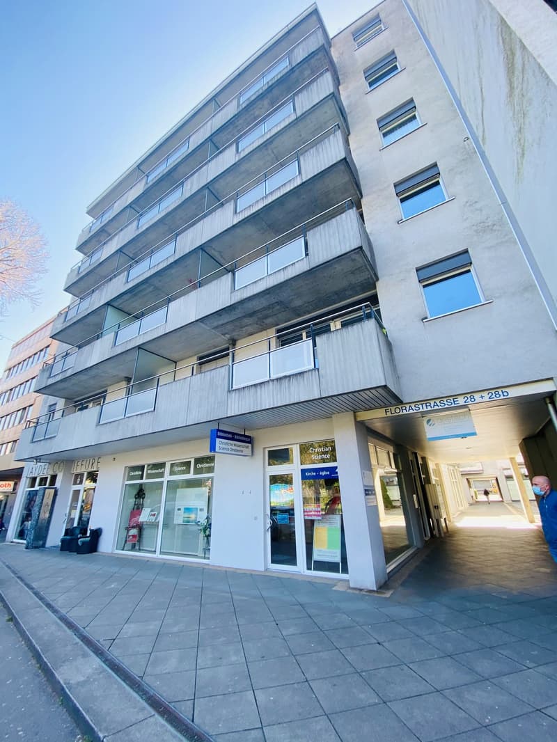 A multistory residential building with balconies, glass doors and windows, and signage indicating stores or offices on the ground floor.