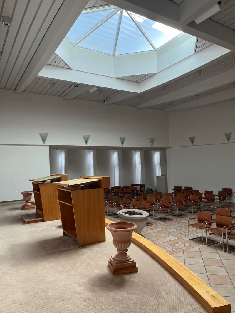 A modern building with rows of chairs, wooden podiums, and a central light well