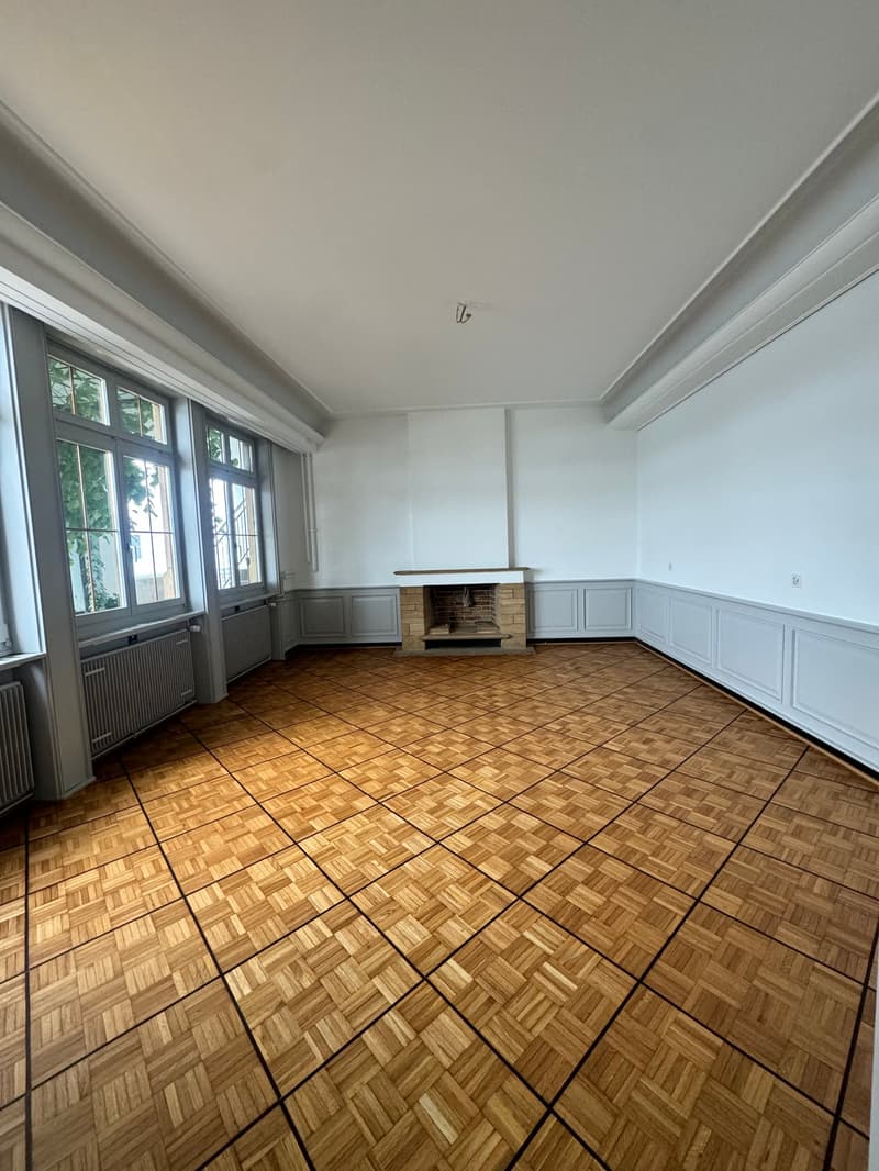 Empty room, wooden floors, brick fireplace, windows, white walls, heaters