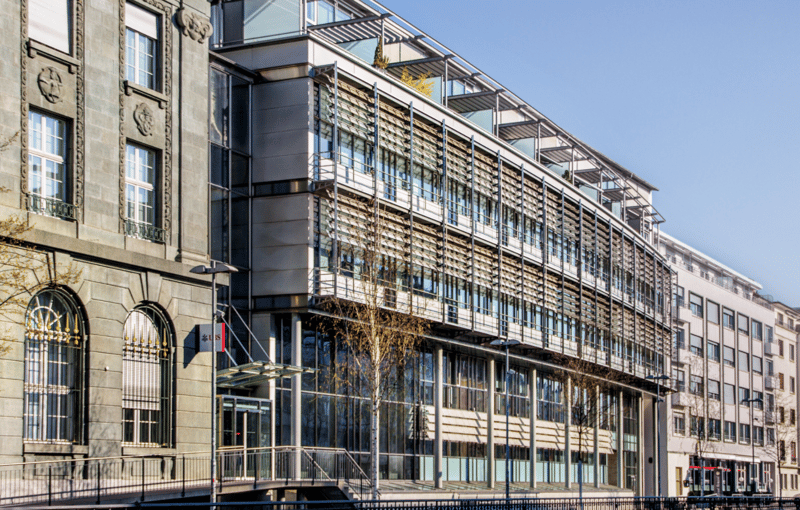 Gray building, large windows, metal railings, balcony, glass entrance, street lamp