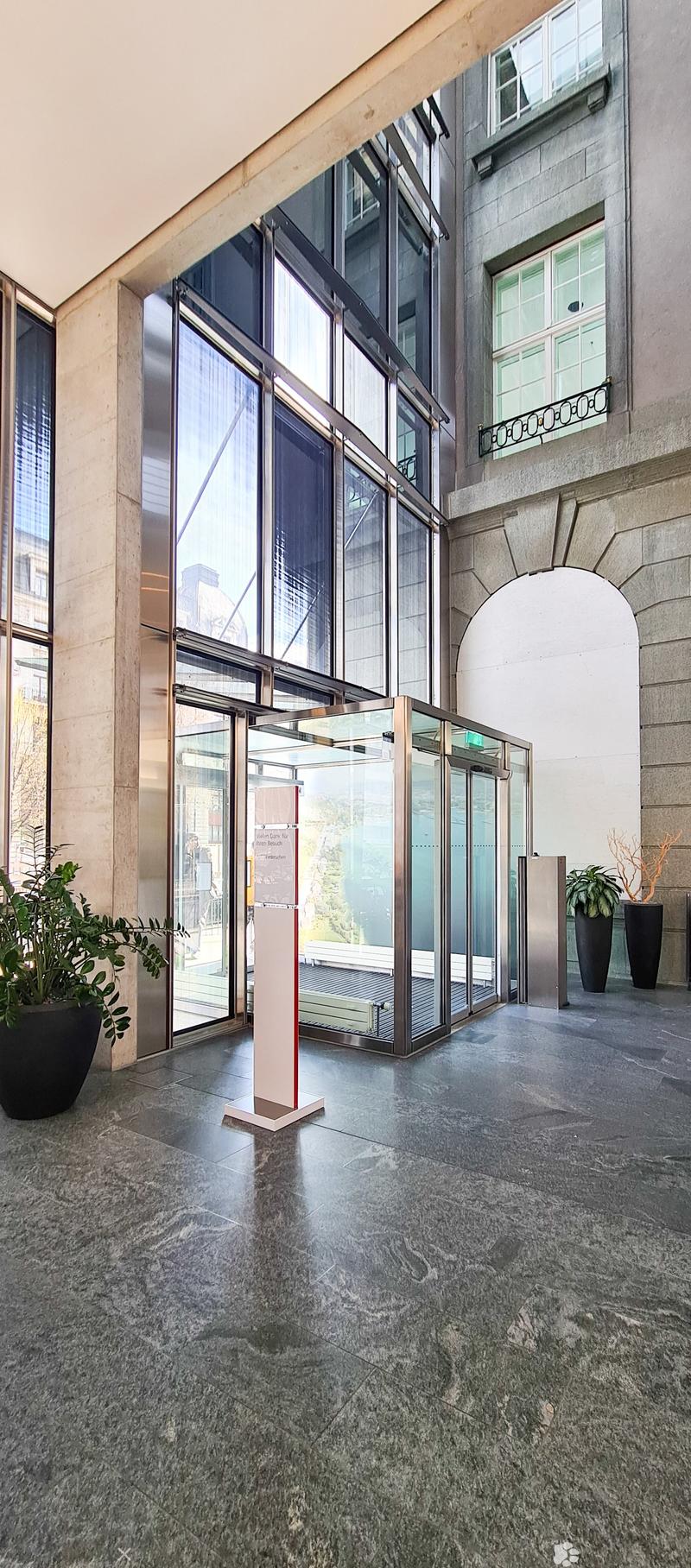 spacious entrance with high ceiling, large glass doors, granite floors, glass walls, two large indoor plants