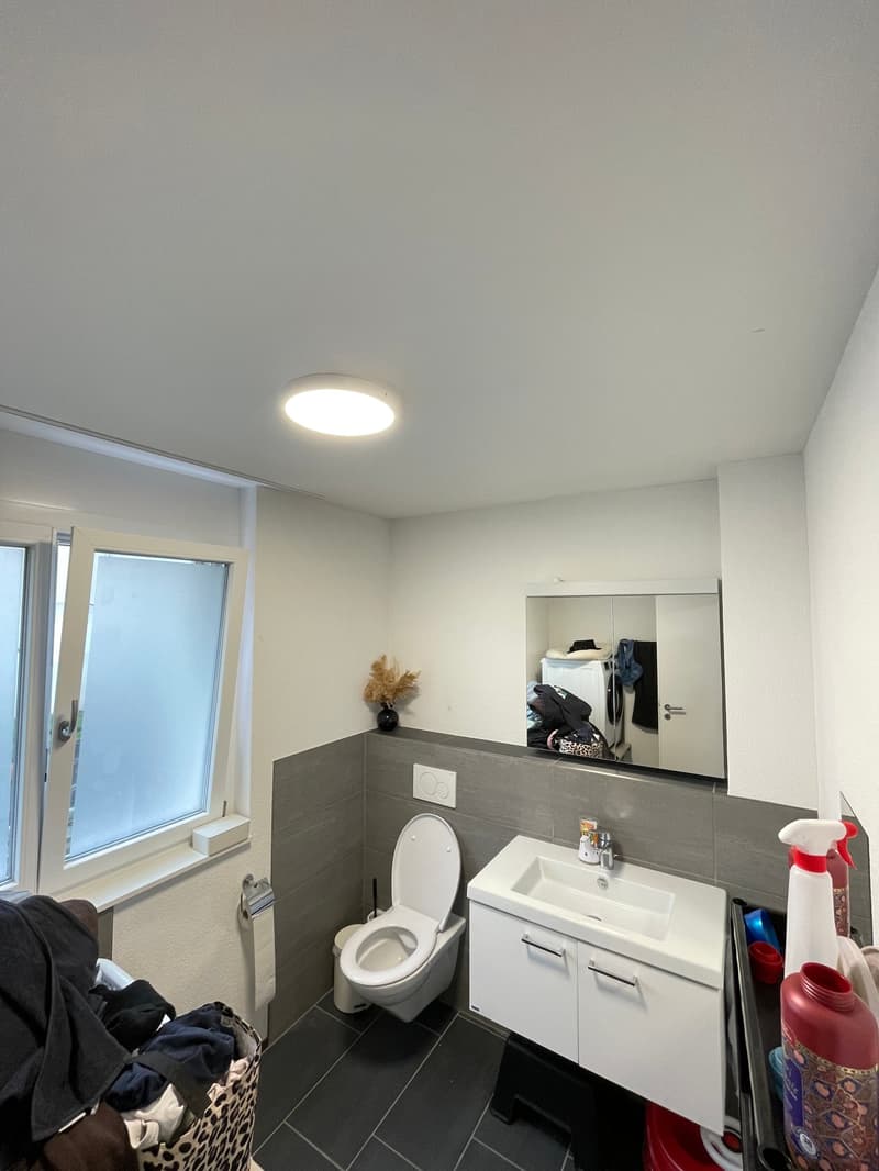 Bathroom with white toilet, sink, mirror, and black tiled floor