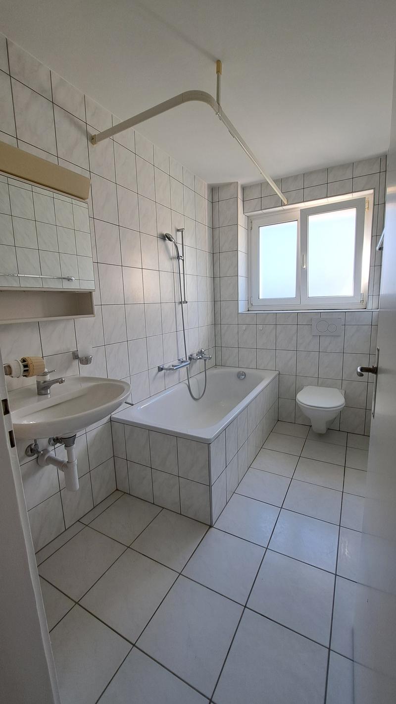 Bathroom with white tiles, bathtub, sink, toilet, shower head, window
