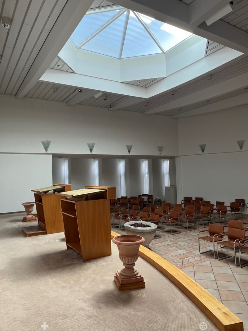 A modern building with rows of chairs, wooden podiums, and a central light well