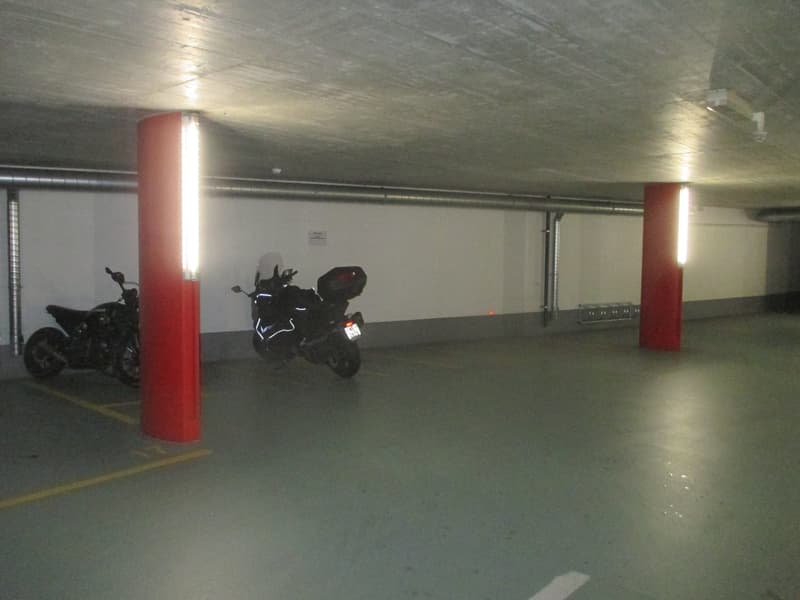 Motorcycles parked in a concrete parking lot with two red columns and overhead lights
