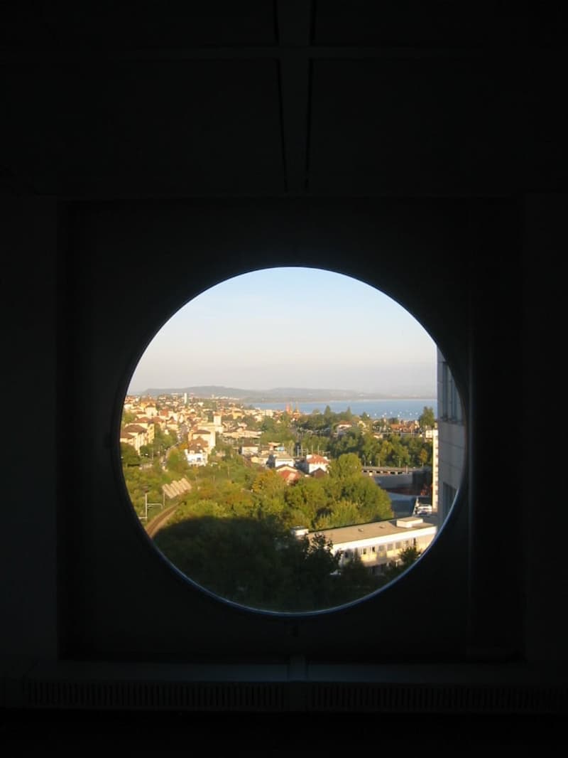 circular window, panoramic view, cityscape, ocean, hills, trees